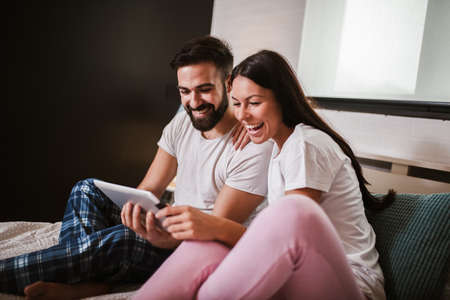 Smiling relaxed young couple using digital tablet in bed at homeの写真素材