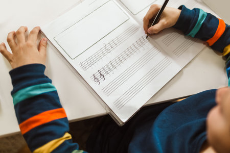 Little boy writes musical notes and violin key at home.