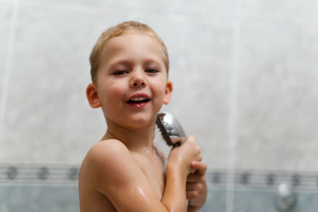 Cute happy smiling funny undressed boy child with blonde hair taking shower in bath with water indoor.の写真素材
