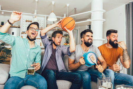 Happy male friends  wearing black face protective mask watching basketball at home