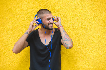 Tattoo man is listening to music using headphones on a yellow wallの写真素材