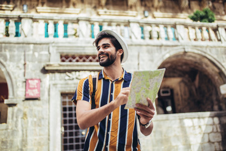 Happy tourist with backpack is making travel across city uses a map for orientation.の写真素材