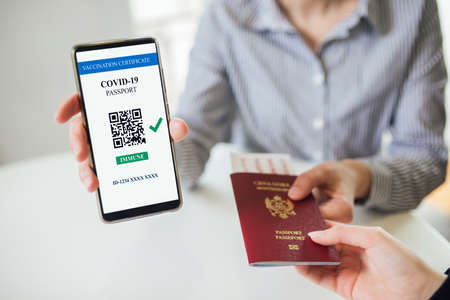 Checking into hotel and passing passport. Smartphone displaying a valid digital vaccination...