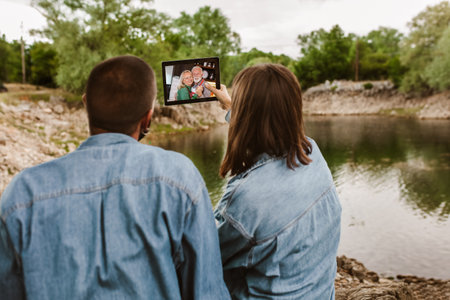 Couple in love camping.Couple sit near the lake and using digital tablet for video call.の写真素材