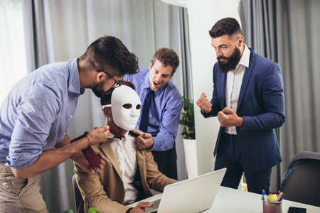 Happy colleagues having fun at meeting in boardroom, sitting at table together, sharing ideas, discussing project strategy. Businessman hidden behind the maskの写真素材