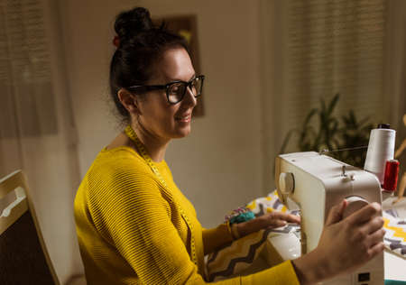 Woman sewing on a sewing machine at her home. Woman seamstress work on the sewing-machine