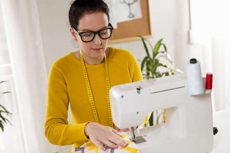 Woman sewing on a sewing machine at her home. Woman seamstress work on the sewing-machineの写真素材