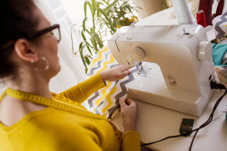 Woman sewing on a sewing machine at her home. Woman seamstress work on the sewing-machine
