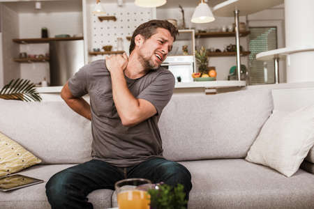 Unhappy man suffering from neck pain at home