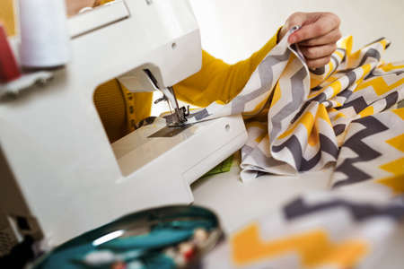 Woman sewing on a sewing machine at her home, close up.