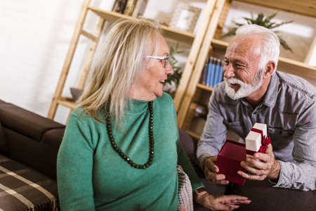 Senior man giving a present to his woman at home.の写真素材