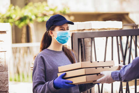 Pizza delivery girl carrying pizza boxes wearing protective mask to an elderly person.