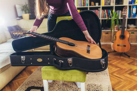 Woman observes and putting a classic brown guitar from a black caseの写真素材