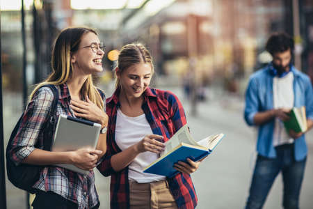 Happy young university students friends studying with books and digital tablet at universityの写真素材