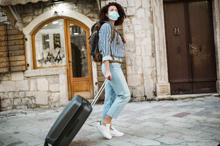 New normal of traveler. Beautiful woman travel in holiday with backpack and suitcase and wearing protection mask virus for safety tripの写真素材