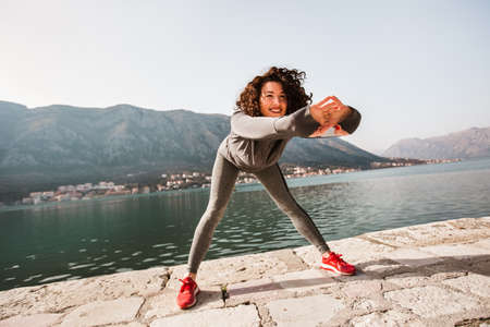 Athletic young woman with curly hair doing exercises on the beach