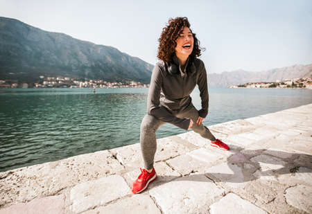 Athletic young woman with curly hair doing exercises on the beachの写真素材