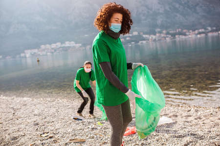 Female volunteers clean beach from garbage, plastic, hold green trash bags and care of environment.の写真素材