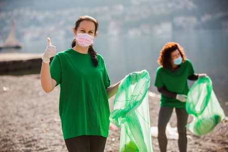 Female volunteers clean beach from garbage, plastic, hold green trash bags and care of environment.の写真素材