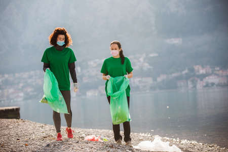 Female volunteers clean beach from garbage, plastic, hold green trash bags and care of environment.の写真素材