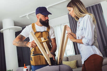 Wife helping husband to repair broken chair at homeの写真素材