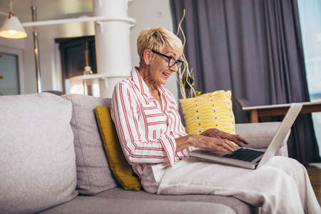 Happy mature woman waving to someone while having a video call over laptop at home.