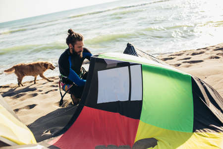 Young man professional surfer standing on the sandy beach with his kiteの写真素材