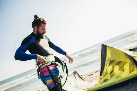 Young man professional surfer standing on the sandy beach with his kiteの写真素材