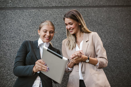 Caucasian woman assistant showing something on tablet device to businesswoman, talking and discussing work.の写真素材