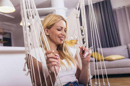Portrait of beautiful young woman posing on swing with glass of wine.の写真素材