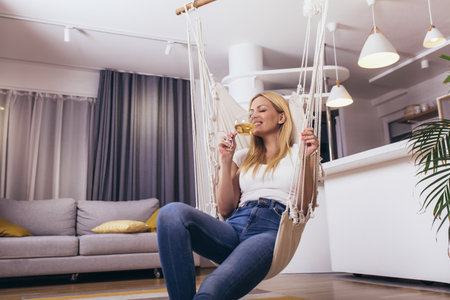 Portrait of beautiful young woman posing on swing with glass of wine.の写真素材
