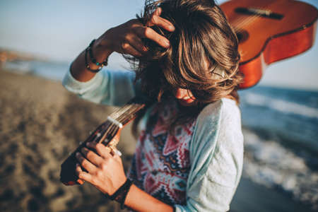 Young woman with guitar on the beach in sunset