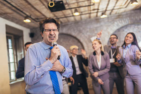 Business people having a karaoke party at the office, singing, dancing and having fun while taking a...