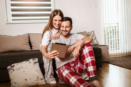 Young couple watching media content online in a tablet sitting on a sofa in the living room.