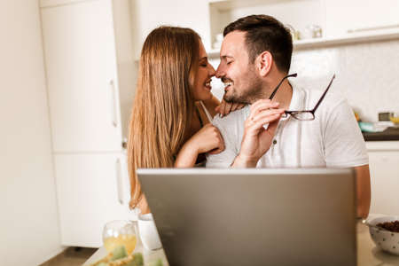 Young couple spending time together at home in the kitchen using laptop.