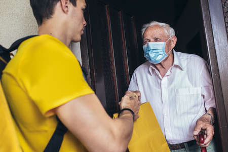 Young male volunteer in mask delivering shopping to senior man. Donation