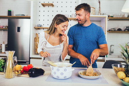 Beautiful young couple is talking and smiling while cooking healthy food in kitchen at home.の写真素材