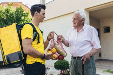 Young male volunteer delivering shopping to senior man. Donationの写真素材