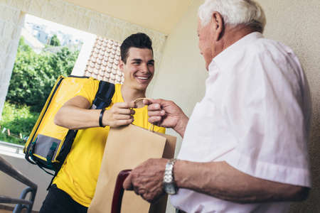 Young male volunteer delivering shopping to senior man. Donationの写真素材