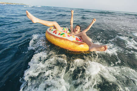 Joyful child on inflatable ring ride on breaking wave. Travel lifestyle, swimming activities. Selective focusの写真素材
