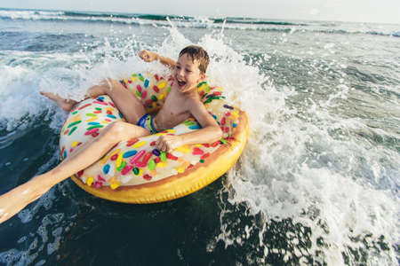 Joyful child on inflatable ring ride on breaking wave. Travel lifestyle, swimming activities....