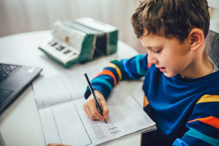 Little boy writes musical notes and violin key at home.