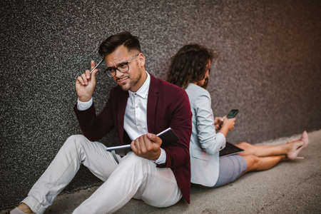 Young business people sitting down in front of a modern office buildingの写真素材