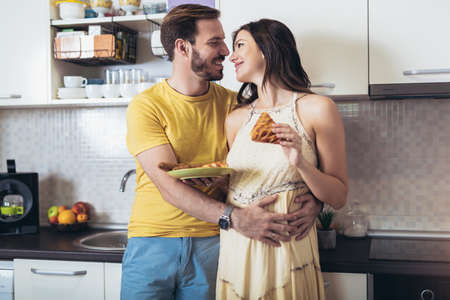 Pregnant woman with husband in the kitchen having fun.の写真素材