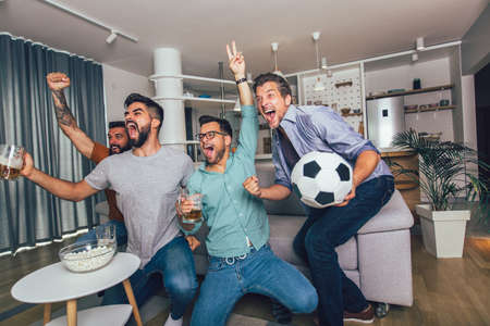 Happy male friends or football fans watching soccer on tv and celebrating victory at home.