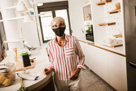 Seniors woman wearing medical face mask at home in the kitchen.Quarantine. Health concept.の写真素材