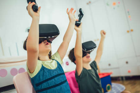 Little kids in virtual reality headsets playing video game at home
