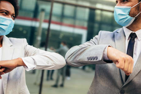Business man and woman with safety masks greeting with elbow bump in front of office building.