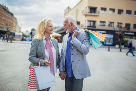 Happy mature couple walking with their shopping purchases on a sunny dayの写真素材