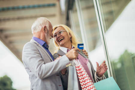 Senior couple carrying shopping bags and enjoying to shopping using credit cardの写真素材